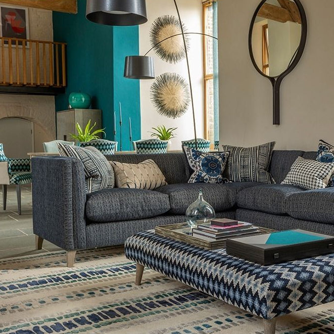 Gray sectional sofa with patterned ottoman in a living room setting.